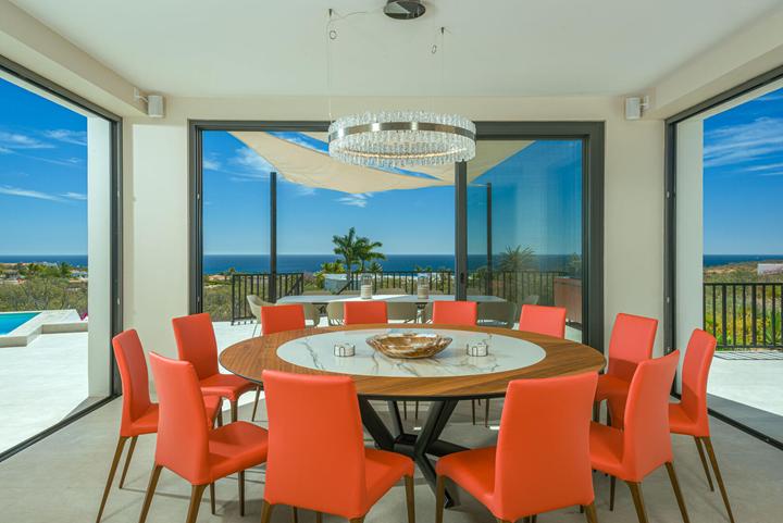Dining room at Casa Alba with a round table, orange chairs and floor-to-ceiling windows facing the sea