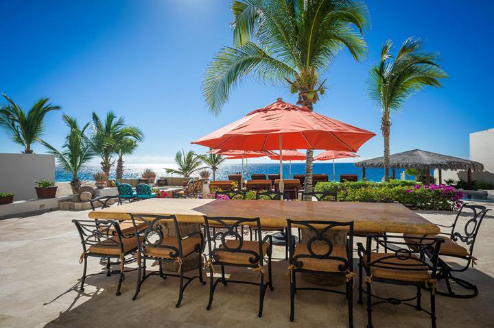 Outdoor dining table for a large group under red umbrellas and palms at Casa Alcini