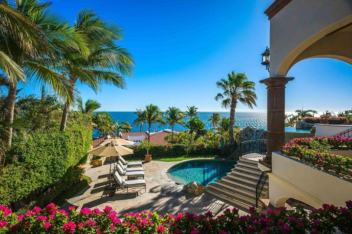 View through a stone arch to the pool, gardens and ocean at Casa Alegria