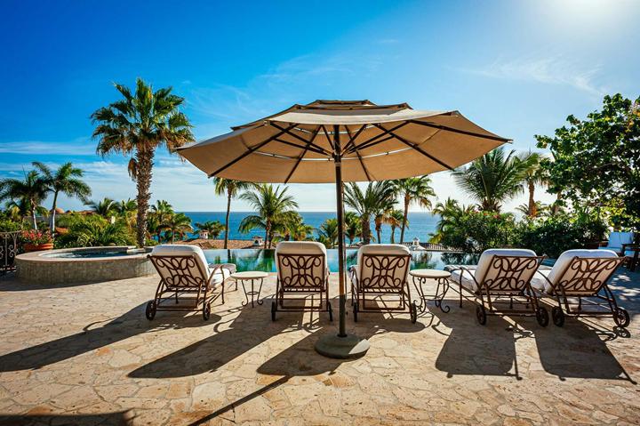 Loungers under a large umbrella overlooking the pool and sea at Casa de las Risas