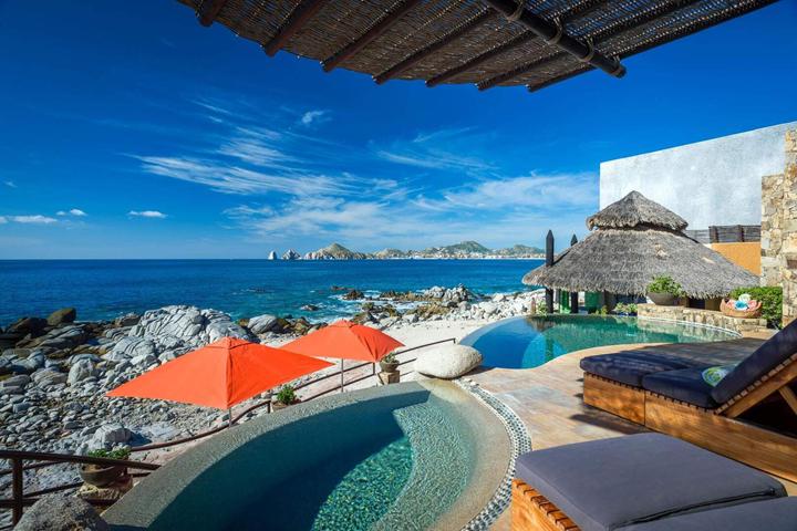Pool, palapa and red umbrellas beside the rocky shoreline at Casa del Arco