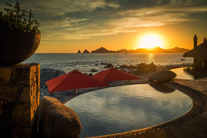 Sunset over a villa pool with the Land's End rock formations beyond